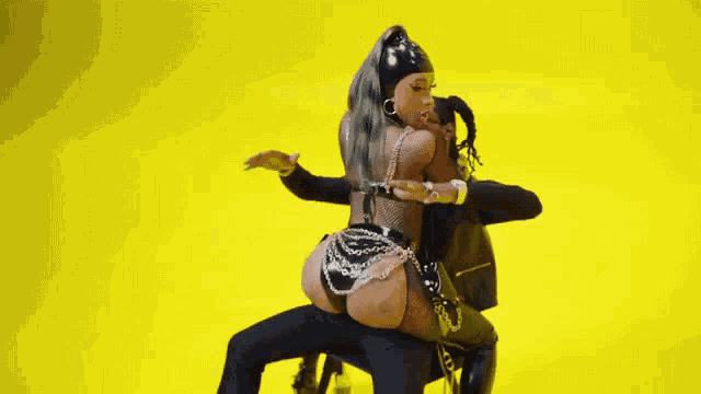 a woman in a bikini is sitting on a man 's lap and dancing on a yellow background .