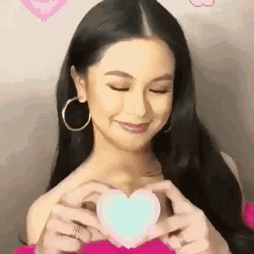 a woman is making a heart shape with her hands while wearing hoop earrings