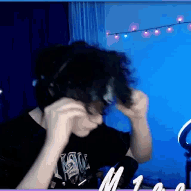 a man wearing headphones is brushing his hair in a room with a blue wall .