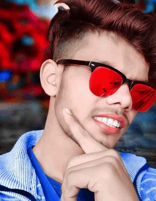 a young man wearing red sunglasses and a blue shirt smiles
