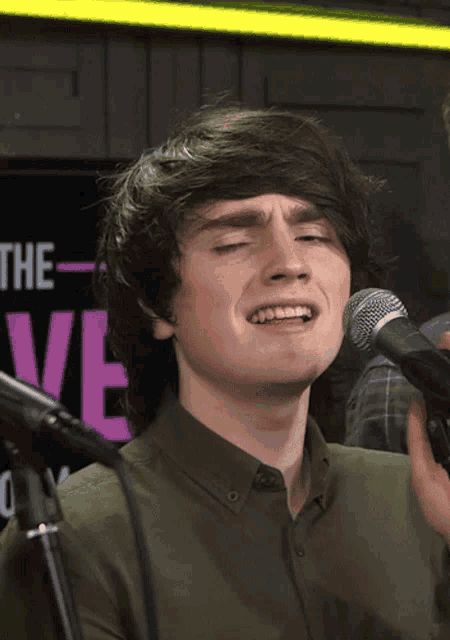 a young man singing into a microphone in front of a sign that says " the "