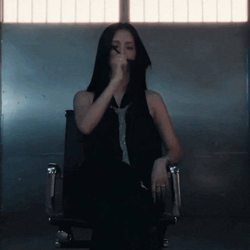 a woman with long black hair is sitting in a chair covering her face