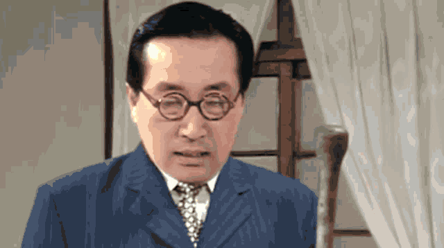 a man in a suit and tie with round glasses looks at the camera