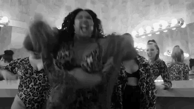 a black and white photo of a woman in a leopard print swimsuit dancing in a dressing room .