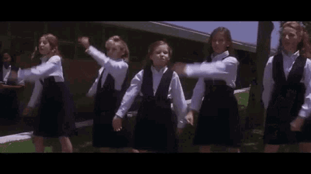 a group of young girls in school uniforms are dancing in front of a school .