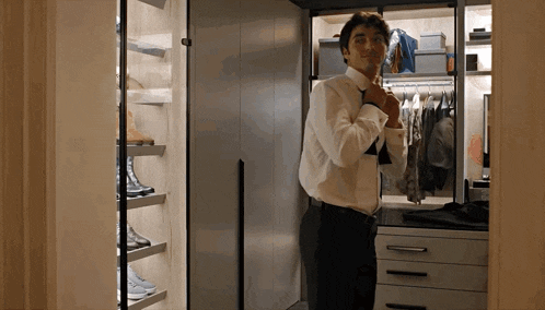 a man in a white shirt and black pants adjusts his tie in a walk in closet