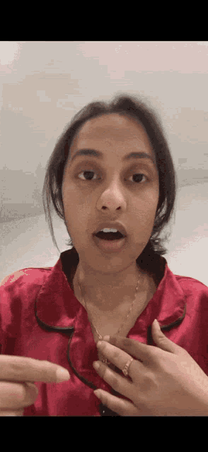 a woman wearing a red shirt and a gold necklace is making a funny face