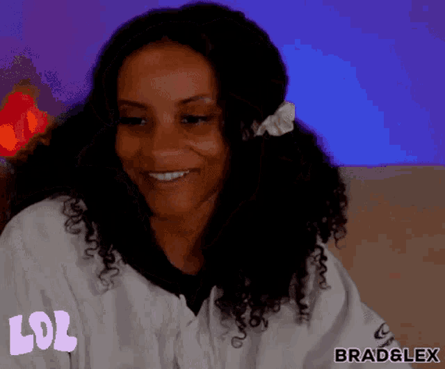 a woman with curly hair is smiling and wearing a white shirt with the word lol written on it .