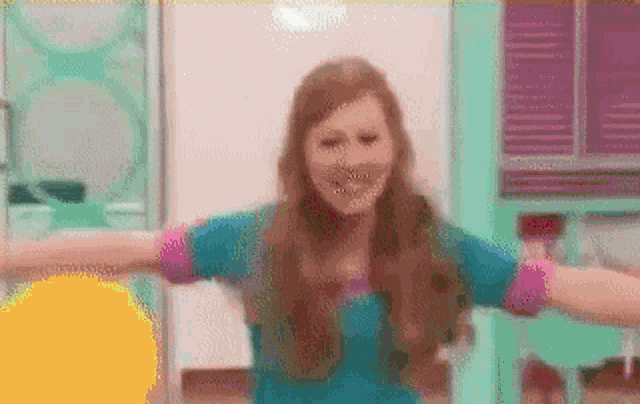 a woman in a blue shirt is dancing with her arms outstretched in a room .
