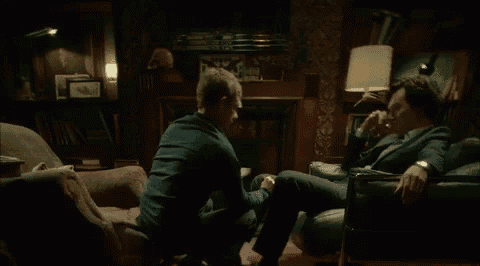 two men are sitting on a couch and one is kneeling down