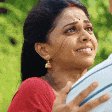 a woman wearing a red shirt and gold earrings looks at the camera