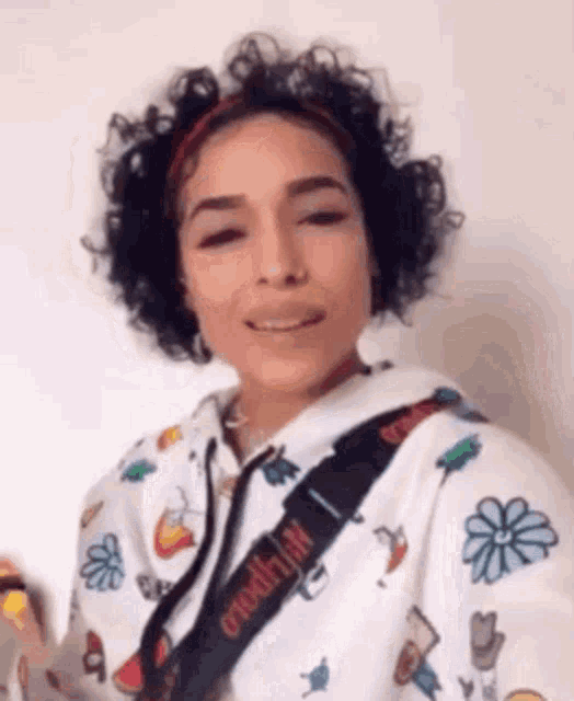 a woman with curly hair is wearing a white hoodie with flowers on it and a headband .