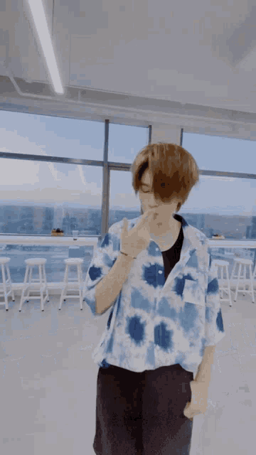 a young man in a blue tie dye shirt stands in front of a window