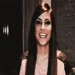 a woman with long hair is smiling and wearing a pink shirt .