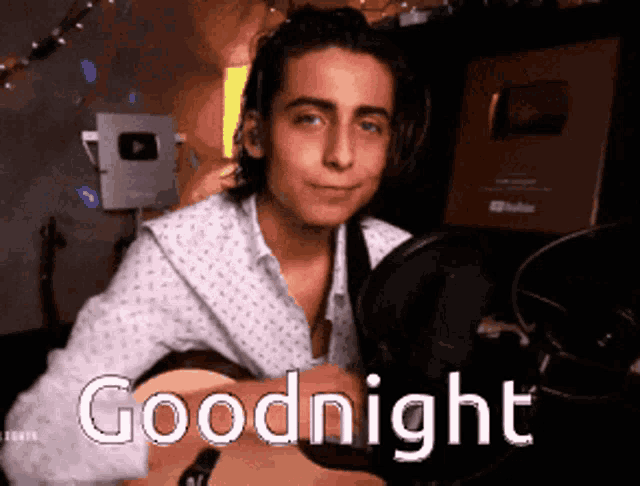 a young man is holding a guitar in front of a microphone and says goodnight .