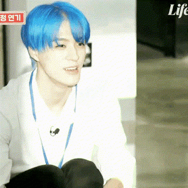 a young man with blue hair and a lanyard around his neck is sitting down .