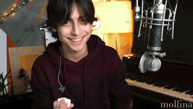 a young man is smiling in front of a piano and a microphone with the name molina on it