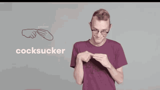 a man wearing glasses and a purple shirt is making a sign that says " cocksucker "