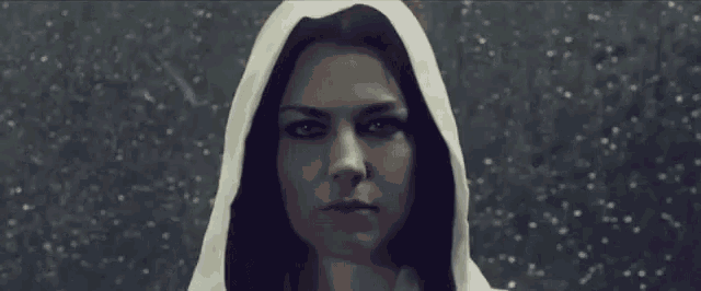 a woman with long black hair and a white hood on her head is looking at the camera .