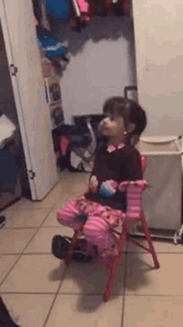 a little girl is sitting on a red chair in a room .