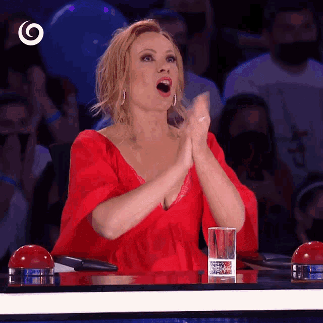 a woman in a red dress sits at a table with a glass of water