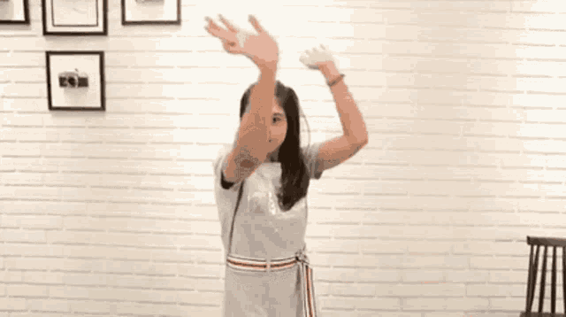 a young woman in a dress is dancing in front of a white brick wall .