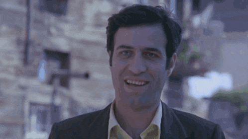 a man in a suit and a yellow shirt smiles