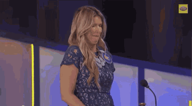 a woman in a blue lace dress is standing in front of a microphone on a stage .