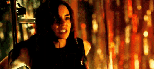 a woman in a black dress is standing in front of a red curtain in a dark room .