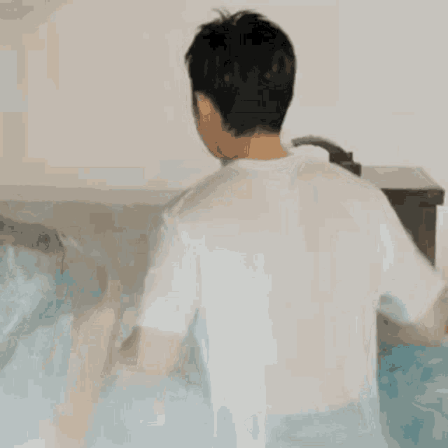 a man in a white shirt is standing in a bathtub with his back to the camera .