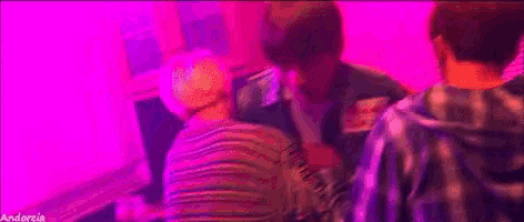 a group of young men are standing next to each other in a room with pink lights .