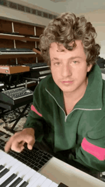 a young man with curly hair is sitting at a piano keyboard