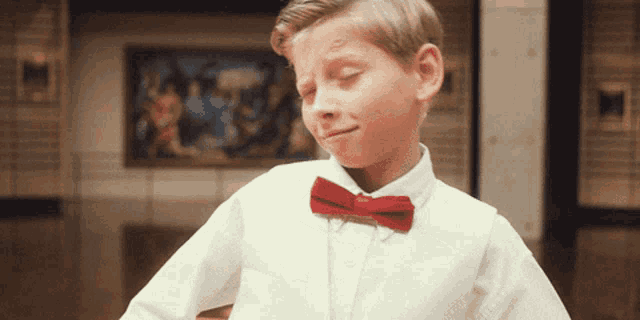 a young boy wearing a white shirt and red bow tie is making a funny face