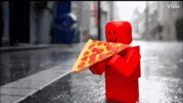 a red lego figure is holding a slice of pizza on a wet street .