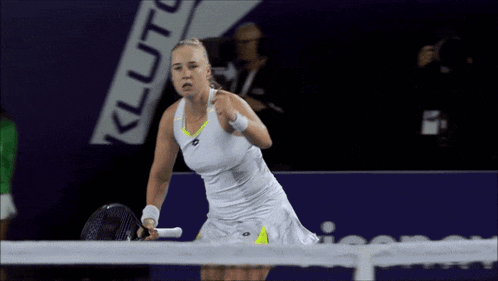 a woman in a white dress holds a tennis racquet in front of a sign that says kluto