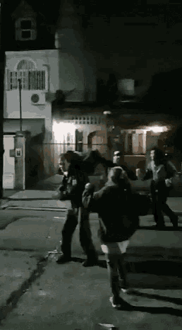 a group of people are walking down a street at night with a building in the background that has the number 8 on it
