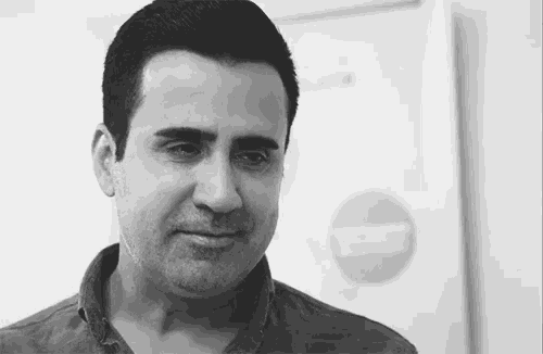 a man is looking at the camera in a black and white photo with a no entry sign in the background .
