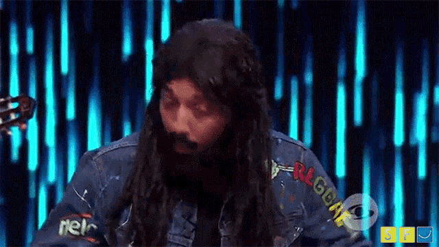 a man with long hair and a beard is wearing a denim jacket that says reggae