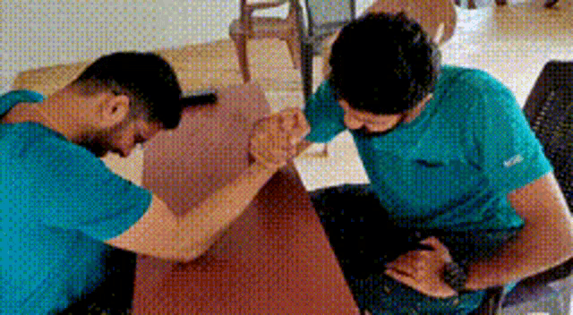 two men in blue shirts are arm wrestling on a table .