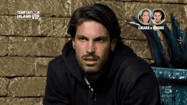 a man sitting in front of a brick wall with temptation island vip written on it
