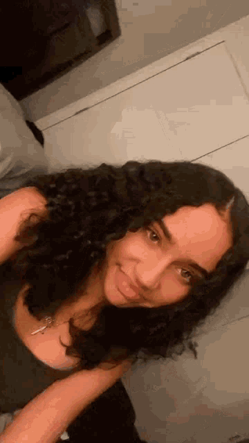 a young woman with curly hair is taking a selfie in a bedroom .