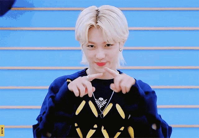 a young boy with blonde hair is wearing a blue sweater and a necklace with the letter v on it