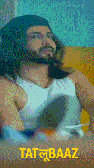 a man with long hair and a beard is wearing a white tank top and a black hat with the word tatbaaz on it