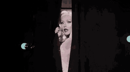 a woman in a pink wig is standing in a dark room .
