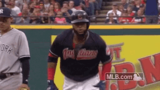 a baseball player wearing an indians jersey runs towards a new york yankees player