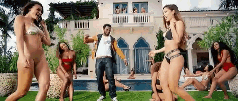 a man is dancing with a group of women in bikinis in front of a large house .