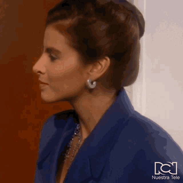 a woman wearing a blue jacket and white earrings with nuestra tele written on the bottom right