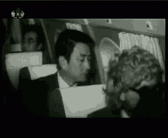 a black and white photo of a man in a suit sitting on a plane