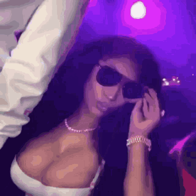 a woman wearing sunglasses and a necklace is standing in a dark room