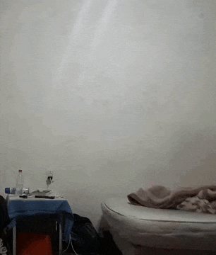a bed with a blanket on it in a room with a table and a wall .